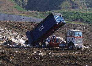 A wide angle view of a garbage truck dumping into a landfill.