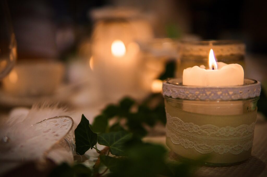 Image of a candle in a lace-wrapped holder with ivy on the table. Other candles are in the distance, blurred. Image by Stefan Nyffenegger from Pixabay
